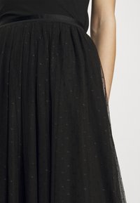 Czarna tiulowa spódnica z teksturowanej tkaniny z małymi, subtelnymi wzorami gwiazd, marszczonym paskiem w talii i przezroczystymi warstwami.