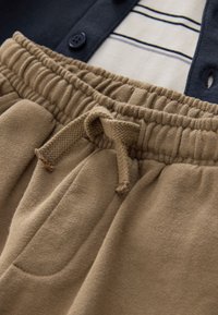 Rugalmas derékpántos rövidnadrág bézs polár anyagból, húzózsinórral. Oldalzsebekkel és puha tapintású felülettel rendelkezik. Rétegezve, egy tengerészkék, gombos ing alatt viselve.