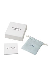 Vit presentask med "SKAGEN DANMARK"-logotyp, ljusblå tygpåse och liten bok. Enkelt design med rena linjer och minimala detaljer.