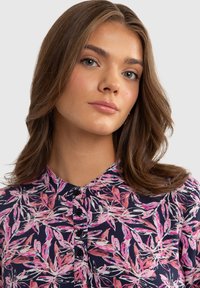 Navy button-up shirt with pink and white leaf pattern, featuring a collar and black buttons. The material appears soft and lightweight.