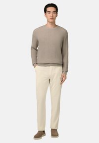 Bež pleteni pulover z rebrastim vzorcem, krema hlače s tapered krojem in taupe slip-on čevlji. Gladke teksture, sproščen kroj in preprost dizajn.