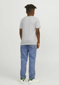 Camiseta de algodón gris, de mangas cortas, con cuello redondo, combinada con jeans de mezclilla azules, zapatillas blancas con acentos verdes, vista desde la parte de atrás.