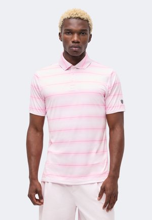 Junger Mann mit kurzen blonden Haaren, der ein hellrosa Poloshirt mit dünnen horizontalen Streifen und passende hellrosa Shorts trägt.