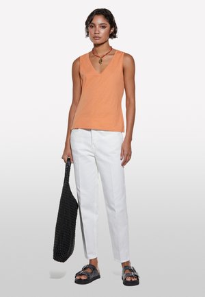 Orange sleeveless top with a V-neck, paired with white straight-leg pants and black flat sandals. Black woven tote bag.
