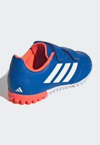 Blue athletic shoe with white stripes, featuring a velcro strap and a textured sole in bright orange. Interior lining is also orange.