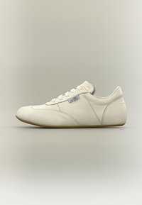 Λευκό δερμάτινο sneaker χαμηλού ύψους με δέσιμο μπροστά, ορατές ραφές και μικρή ορθογώνια ετικέτα με λογότυπο στο πλάι, εμφανίζεται σε προφίλ πλευράς.