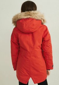 Czerwony pikowany parka z futrzanym kapturem, z troczkiem w talii, długimi rękawami i bocznymi kieszeniami. Gładka faktura z eleganckim wzornictwem.