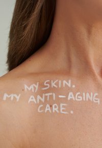 Text in Weiß auf heller Haut liest: "MEINE HAUT. MEINE HAUTPFLEGE GEGEN ALTERUNG." Die Hautoberfläche ist glatt mit einigen natürlichen Texturen.
