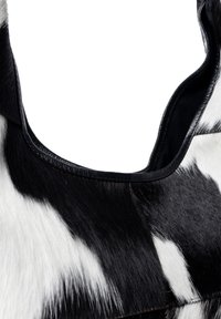 Kossy shoulder bag i koskind med ett svart och vitt mönster, med mjuk, texturerad päls och en slät läderkant längs kanterna.