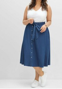 Džínová sukně s přiléhavým pasem, zavazovacím detailem a zapínáním na knoflíky vpředu. Sukně má délku ke kolenům a klasickou modrou barvu.