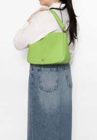 Groene leren schoudertas met een afgeronde vorm, een gladde textuur en een klepsluiting. Voorzien van een korte schouderband en een goudkleurige drukknoop.