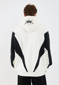 Overmaat hoodie in wit en zwart fleece, met een gedurfde zwarte grafiek op de capuchon, contrasterend paneelontwerp en ribgebreide manchetten.