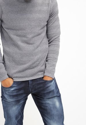 Gray textured long-sleeve shirt with horizontal stripes, paired with dark blue denim jeans featuring slight distressing and a fitted design.