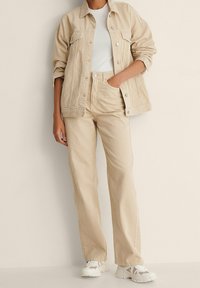 Chaqueta de mezclilla beige con cierre de botones, combinada con una blusa beige a juego y pantalones beige de tiro alto y corte recto. Incluye zapatillas blancas.