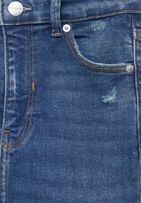 Gros plan sur la poche avant d'un jean en denim bleu avec rivets métalliques, coutures orange et légers détails usés près du bord de la poche.