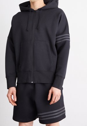 Svart zip-up hoodie med framfickor, dragsko för huvan och horisontella randiga detaljer. Kombinerad med svarta shorts med randiga detaljer.