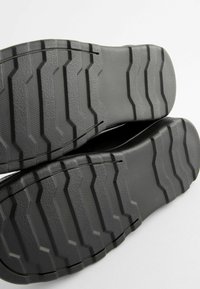 Schwarze Schuhsohlen mit einem strukturierten, zickzackförmigen Profil für besseren Grip, ausgestattet mit einer glatten Kante und ausgeprägten Rillen für Haltbarkeit.