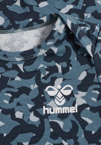 Blaues Oberteil mit Tarnmuster und kurzen Ärmeln, das ein weißes "hummel"-Logo trägt. Der Ausschnitt ist gerippt und hat eine glatte Textur.