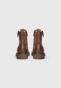 Ett par bruna läderankelboots med siddragkedjor, fleecefoder och robusta sulor, visade framifrån mot en enkel bakgrund.