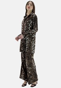 Camicia in satin con stampa leopardata e pantaloni a gamba larga in marrone e crema. Camicia con bottoni e colletto; tessuto strutturato e liscio; abbinata a tacchi neri con cinturini.