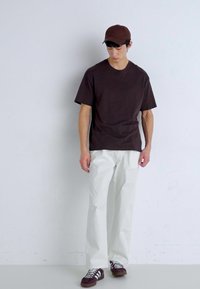 Bruine T-shirt met korte mouwen gecombineerd met witte recht gesneden broek en bruine sneakers. Eenvoudig ontwerp zonder zichtbare patronen of hardware.