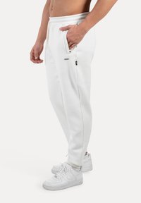 Pantalones de chándal blancos con cintura ajustable, bolsillos laterales y un corte ajustado. Se combinan con zapatillas blancas con acentos negros simples.