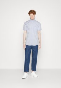 Chemise à manches courtes en vichy bleu clair avec un col italien, associée à un jean bleu foncé ajusté et des baskets blanches.