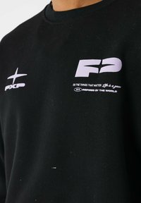 Sweatshirt noir avec un logo "F2" blanc et le texte "Faites les choses qui comptent La vie est un jeu 2011 Inspiré par le monde" sur la poitrine.