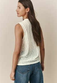 Débardeur crème sans manches avec un motif floral texturé, col rond et tissu doux. Assorti à un jean en denim bleu clair, coupe décontractée.