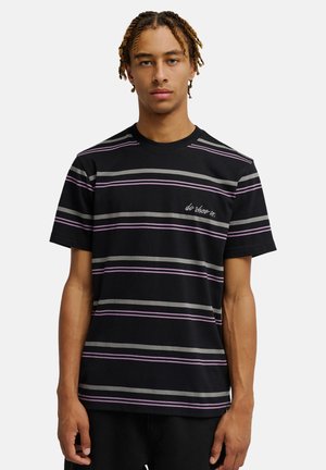 Jeune homme aux cheveux tressés portant un t-shirt noir à rayures horizontales grises et violettes avec un petit texte blanc sur la poitrine.