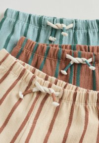 Tři páry pruhovaných šortek: světle modré s tyrkysovými pruhy, terakotové s tyrkysovými pruhy a béžové s hnědými pruhy. Každé mají stahovací pás na šňůrku.