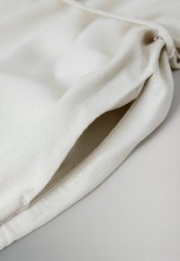 Gros plan sur une pochette en tissu blanc avec une ouverture sur le côté et des coutures discrètes, posée sur une surface unie.