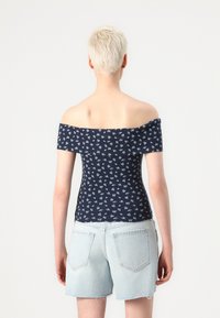 Marine skuldertop med små hvite blomstermønster, tettsittende design og korte ermer; brukt med lyseblå denimshorts.