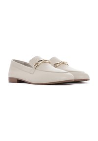 Mocassini in pelle beige con un accento di catena dorata sulla parte superiore, tacco piatto e design a punta. Texture liscia e stile minimalista.