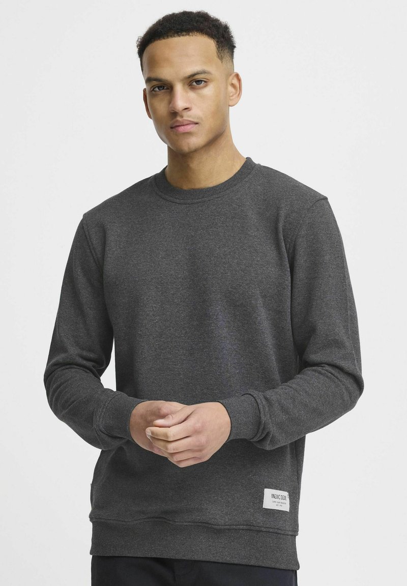 Donkergrijze sweatshirt met een ronde hals, lange mouwen, ribgebreide boorden en onderkant. Heeft een klein label aan de onderkant aan de linkerkant. Gladde textuur.