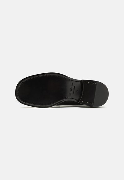 Sole di scarpa in pelle nera con superficie liscia, punta arrotondata e dettagli di cucitura. Presenta un tacco squadrato e rivetti in ottone vicino al tacco.