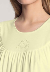 Pigiama di un giallo chiaro con scollatura rotonda. Presenta un ricamo discreto con un design floreale sopra il tessuto arricciato. Texture morbida e liscia.