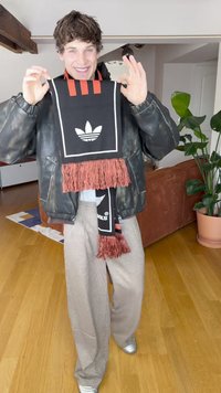 Μαύρο κασκόλ με κόκκινες πινελιές και φούντες, με λευκό λογότυπο Adidas. Φορώντας το με μαύρο δερμάτινο μπουφάν και παντελόνι με σχέδια.