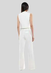 Top corto bianco senza maniche e pantaloni larghi bianchi a vita alta. Tessuto liscio, cuciture minime, zip sul retro e un dettaglio della tasca discreto.