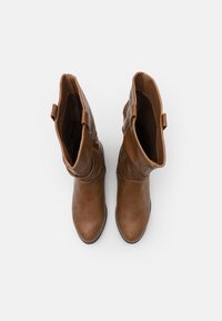 Bottes hautes jusqu'au genou en cuir marron avec une finition lisse, des plis souples et une semelle plate, avec un détail de boucle en haut de la tige.