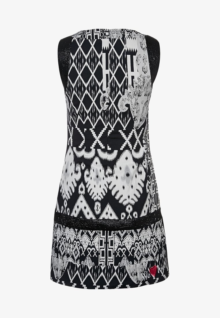 Svart och vit ärmlös tunika med intrikata geometriska mönster, slätt tyg och en spetsdetalj vid nederkanten.