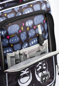 Zaino in tessuto nero con bolle di dialogo colorate e testo. Include tasche grigie per l'organizzazione e una stampa di sneakers sul davanti.