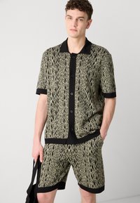Short-sleeve shirt and shorts set in black and green jacquard pattern, featuring a black collar, buttons, and contrasting trim details.