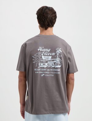 Grijze katoenen t-shirt met een witte grafische afbeelding op de achterkant, met een resort scene, palmbomen en tekst. Korte mouwen, relaxte pasvorm.