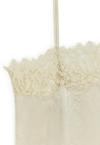 Hellbeige Trägershirt mit einem zarten Spitzenbesatz oben, verstellbaren Trägern und einer glatten, leicht gekräuselten Stoffoberfläche.