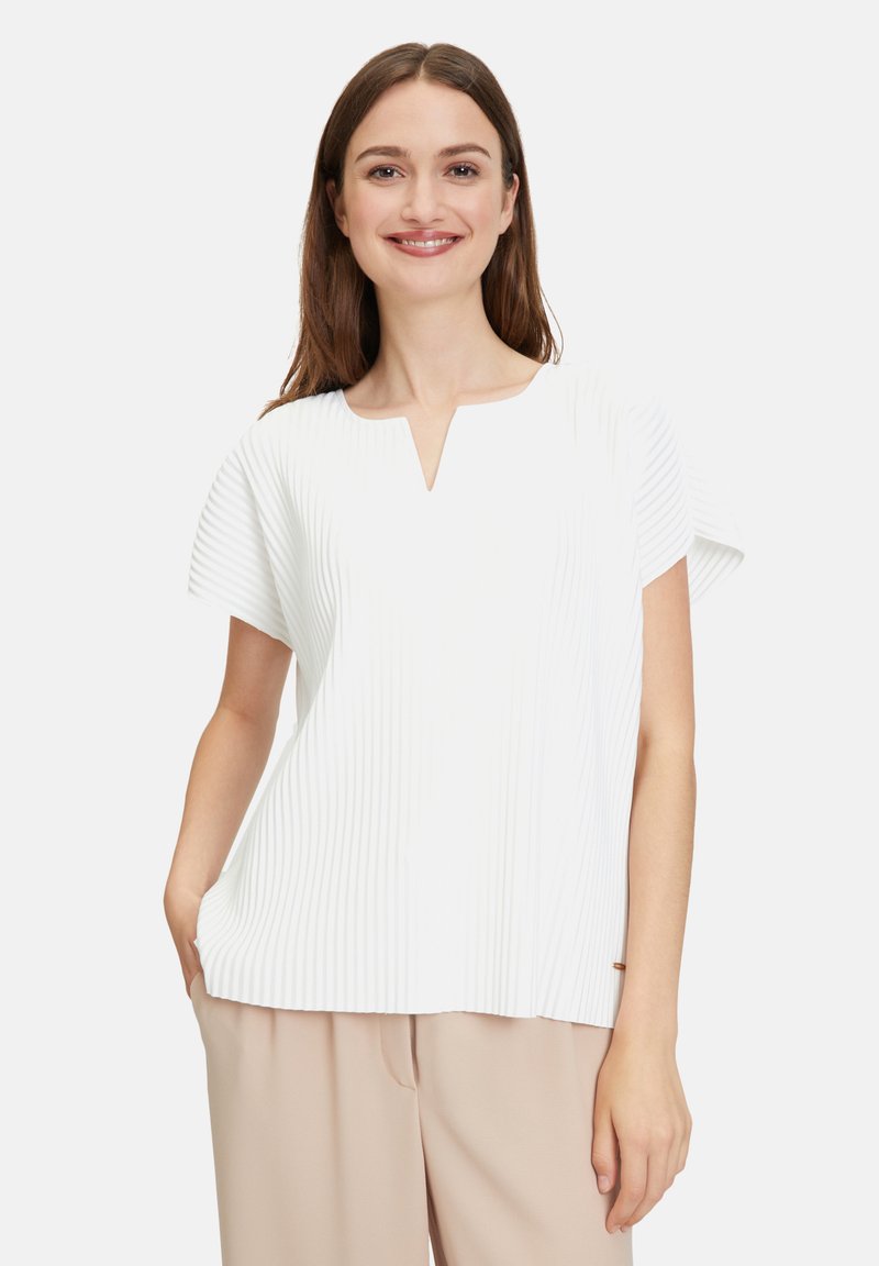 Haut blanc avec des plis verticaux, encolure en V et manches courtes. Le tissu semble léger avec une texture lisse. Présente un subtil détail de couture.