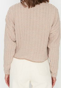 Béžový a bílý pruhovaný svetr s texturovaným pletením, s krátkým designem a dlouhými rukávy. Zadní pohled ukazuje žebrovaný lem a rukávy.