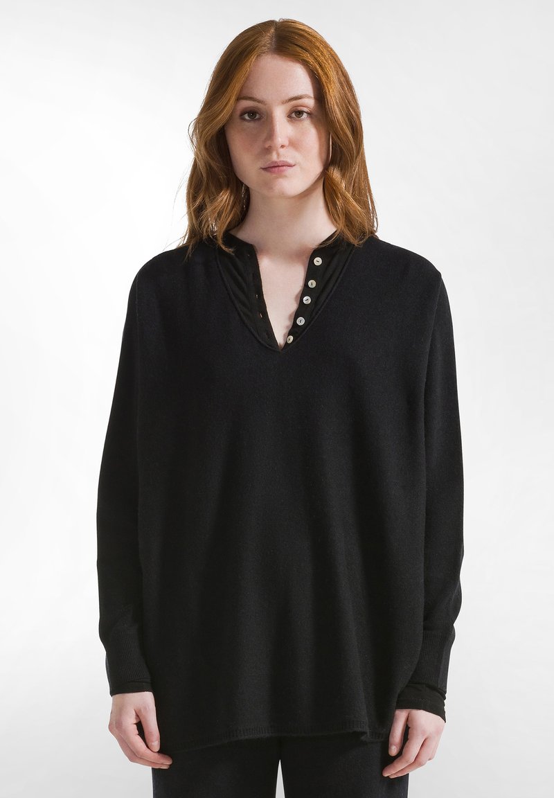 Maglione nero a maniche lunghe con scollatura a V e dettagli di bottoni. Realizzato in tessuto morbido, presenta una vestibilità ampia e polsini a costine.