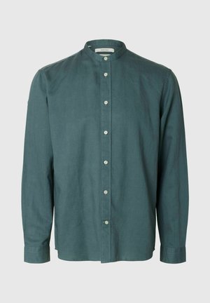 Hosszú ujjú, sötét türkiz zöld gombos ing mandzsetta nélküli gallérral és világos színű gombokkal, semleges háttéren bemutatva.