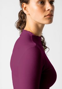 Fialový žebrovaný top s dlouhým rukávem a vysokým volánkovým výstřihem, přiléhavý design a hladká textura, zvýrazňující postavu.